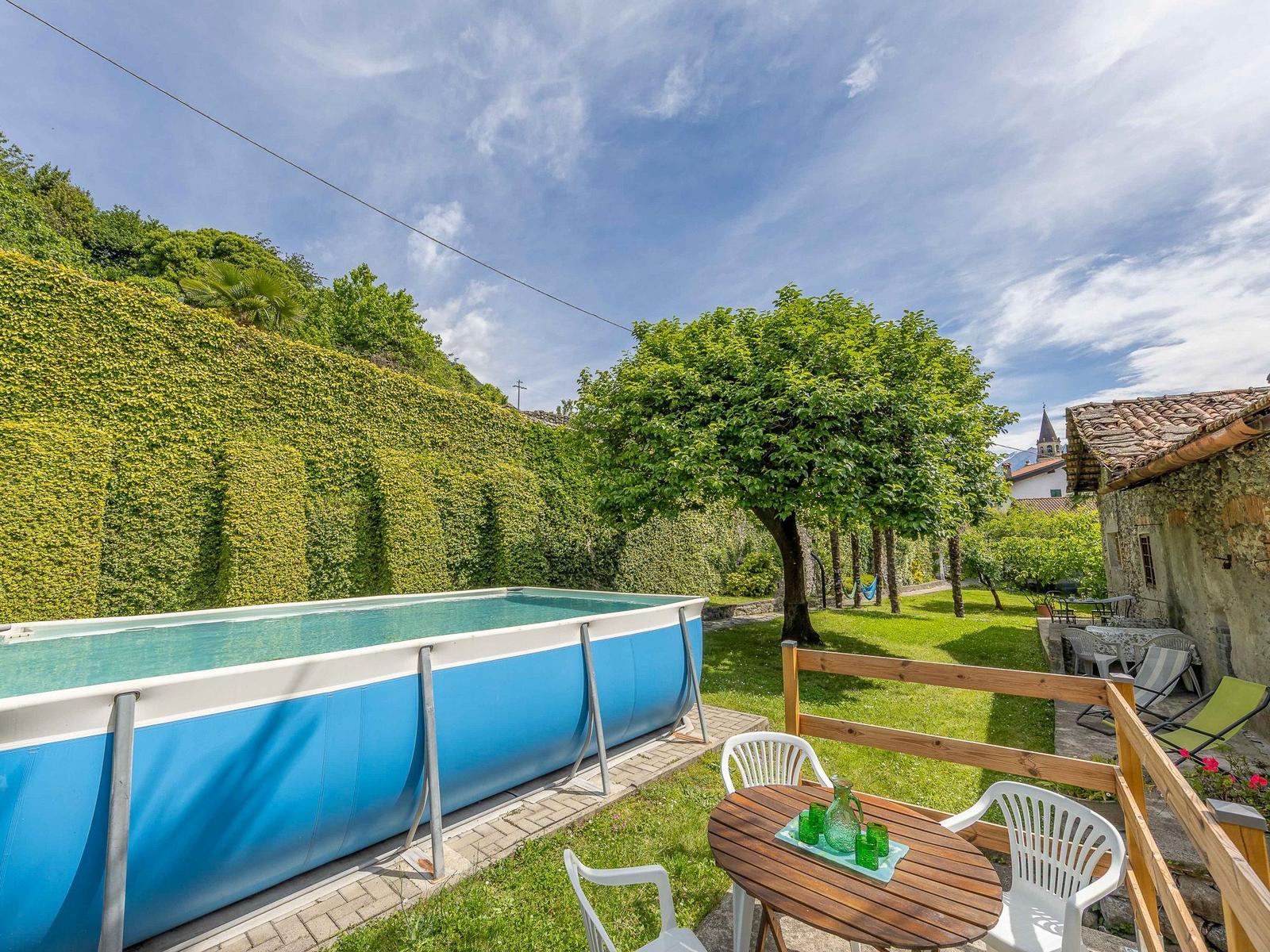 Blauer Pool im Garten mit Tisch, Stühlen und grüner Hecke.