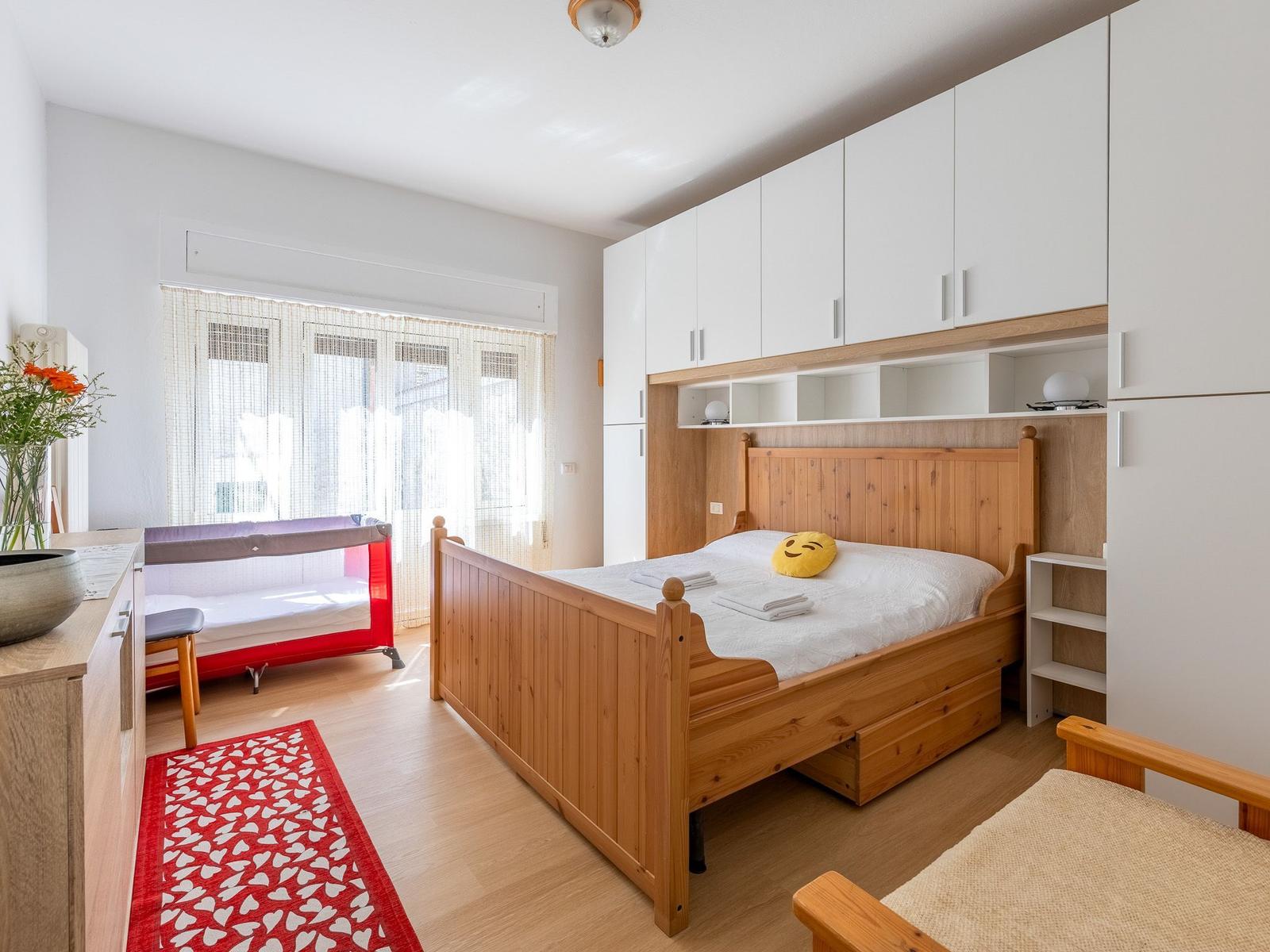 Schlafzimmer mit Holzbett, Babybett und weißen Schränken.