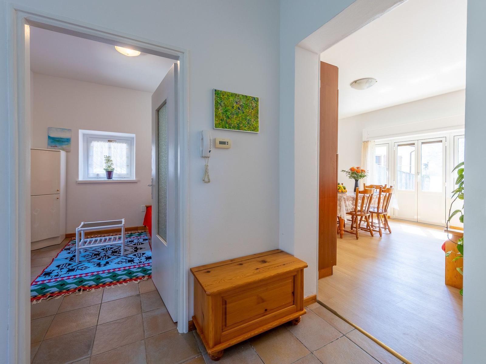 Eingangsbereich mit Holztruhe, Blick in Wohn- und Esszimmer mit Tisch, Stühlen und Fenstern.