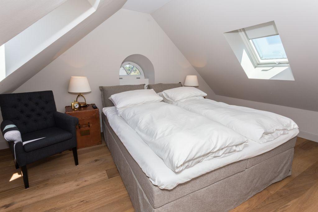 Schlafzimmer mit Dachschrägen, Doppelbett, Sessel und zwei Dachfenstern.