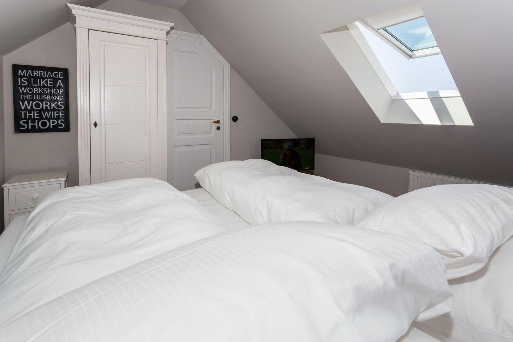 Schlafzimmer mit Dachfenster, Bett und Schrank. Wandbild und Nachttisch sind sichtbar.