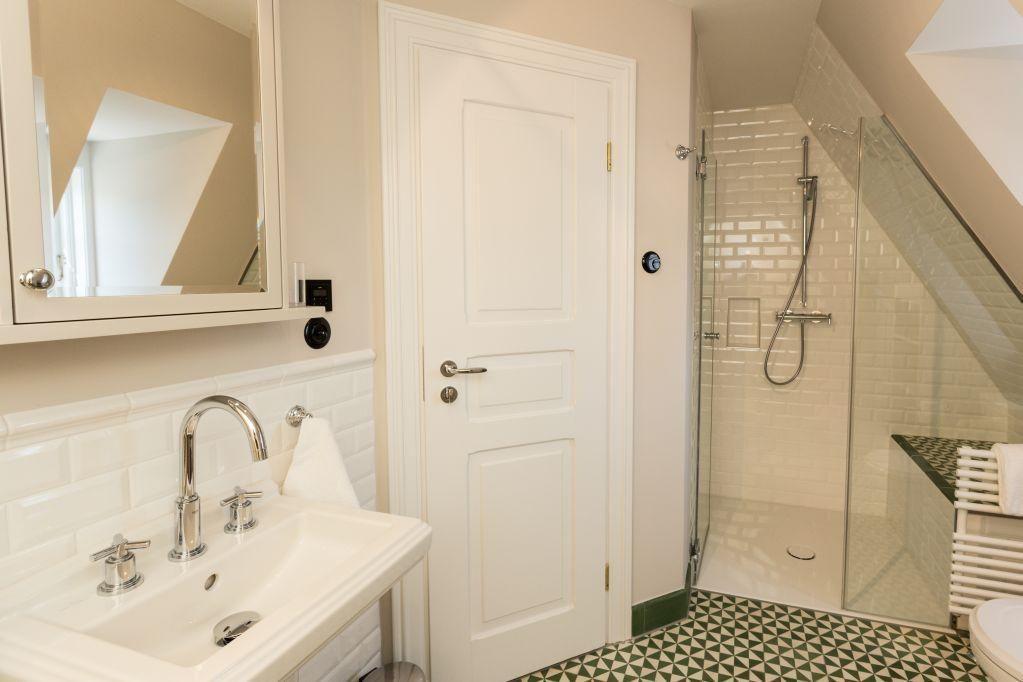 Badezimmer mit Dusche, Waschbecken und Spiegel. Fliesenboden und weiße Wände.