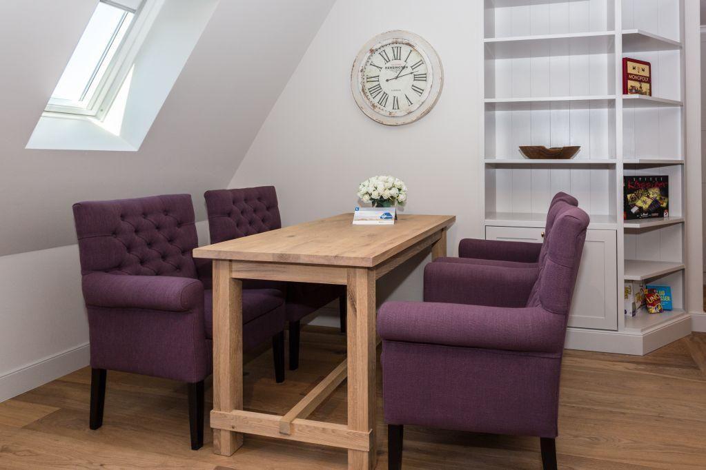 Esszimmer mit Holztisch, vier lila Stühlen, Bücherregal und Dachfenster.