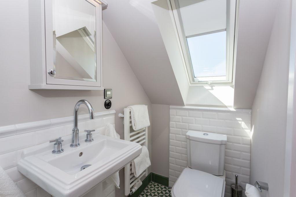 Badezimmer mit Waschbecken, Toilette und Dachfenster. Weiße Fliesen und Handtuchhalter.