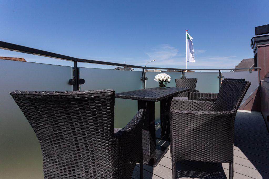 Terrasse mit Tisch und Stühlen, Blick auf Flagge und Himmel.