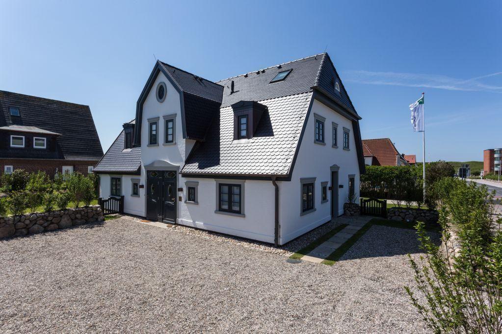 Ein weißes Haus mit schwarzem Dach und Fenstern. Vorhof mit Kies und Grünflächen.