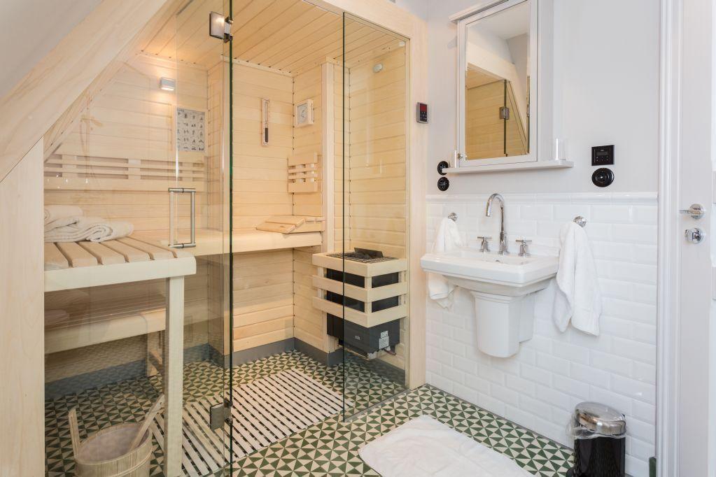 Sauna mit Glaswand, Waschbecken und Fliesenboden.