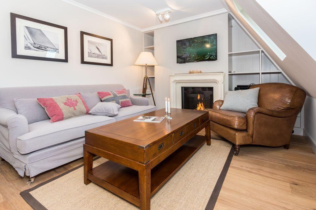 Wohnzimmer mit Sofa, Ledersessel, Kamin und Fernseher unter Dachschräge.