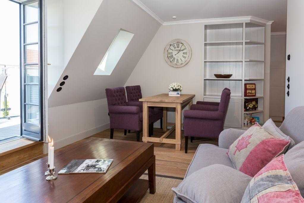 Wohnbereich mit Sofa, Tisch und Stühlen unter Dachschräge mit Fenster und Bücherregal.