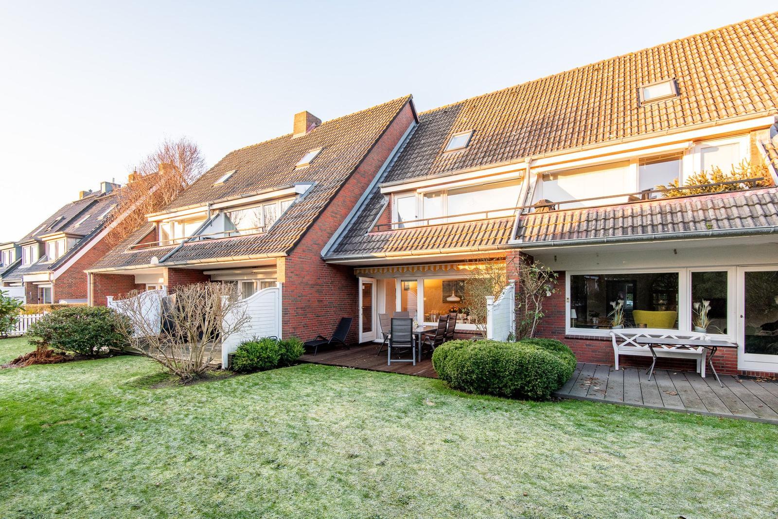 Rotes Backsteinhaus mit Terrasse und Garten. Holzterrasse mit Sitzgelegenheiten.