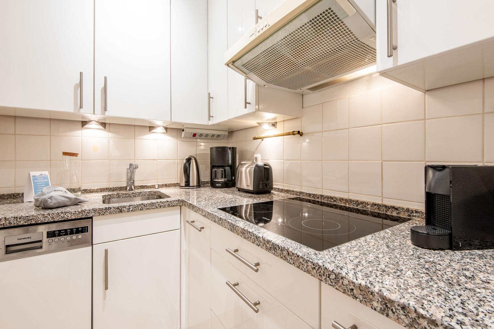 Küche mit Spüle, Kochfeld, Dunstabzug und Küchenutensilien.