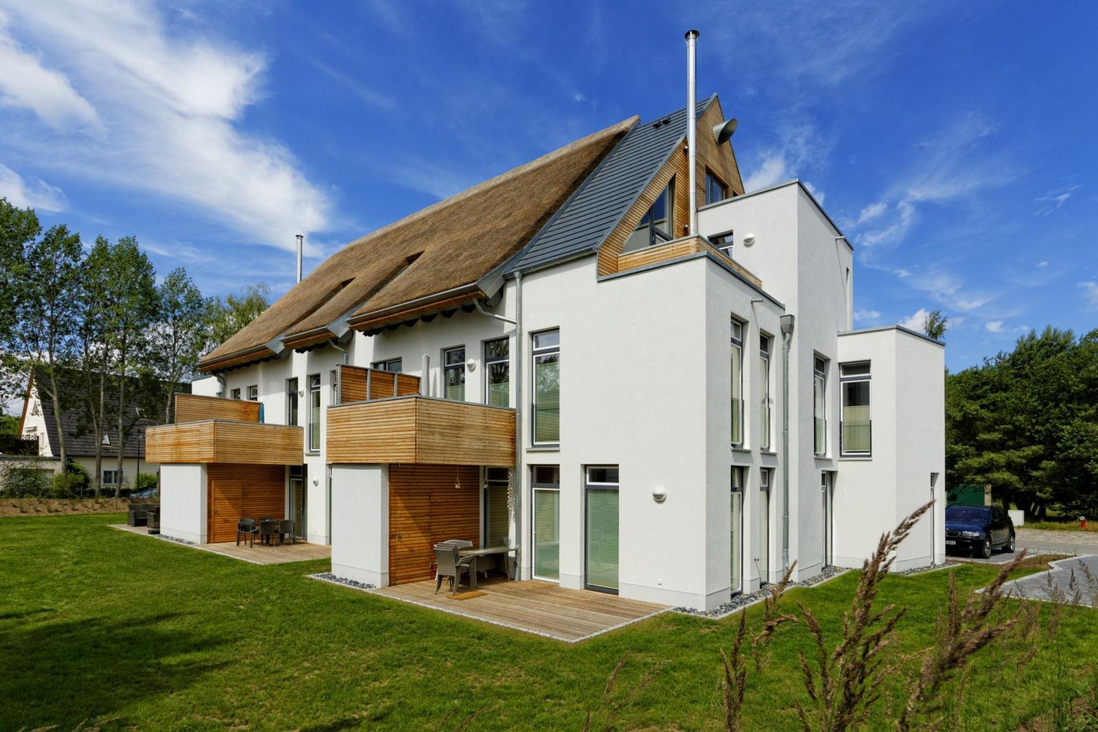 Moderne Villa mit Holzterrasse und grünem Garten unter blauem Himmel.