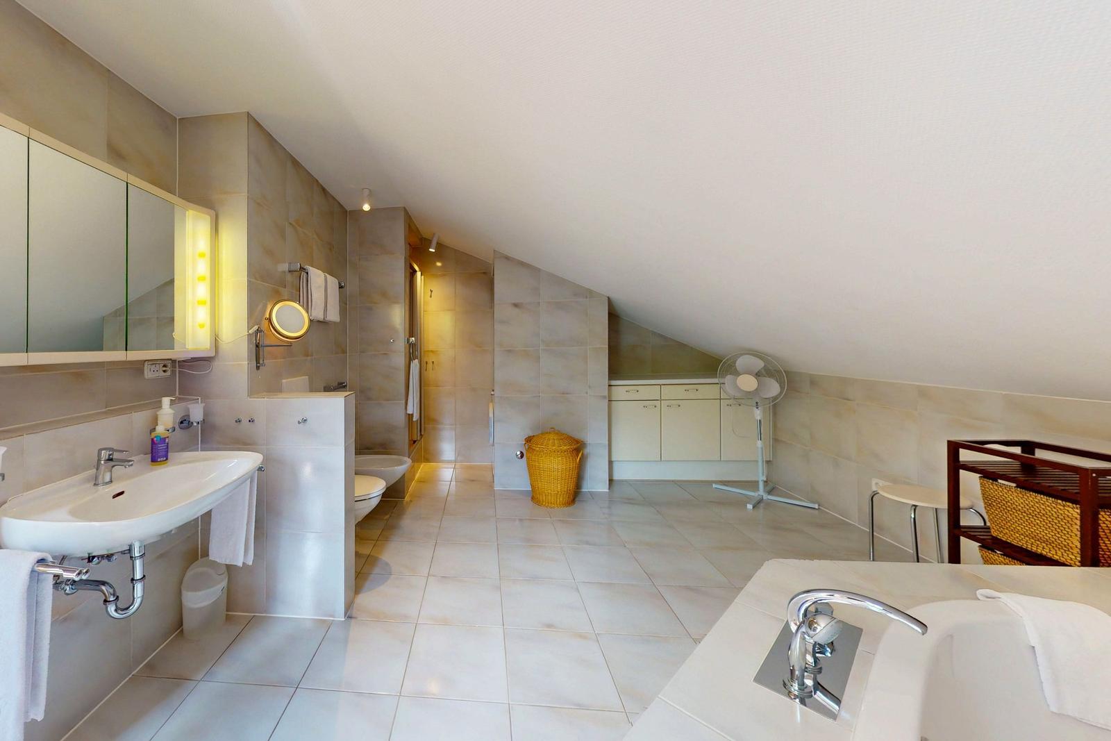 Badezimmer mit Badewanne, Waschbecken und Dusche unter Dachschrägen.