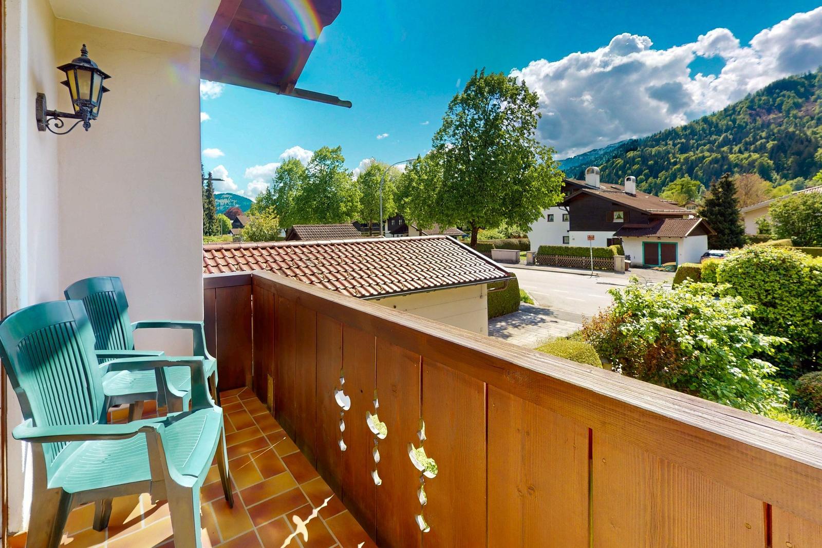 Terrasse mit zwei grünen Stühlen und Holzgeländer. Blick auf Haus und grüne Berge.