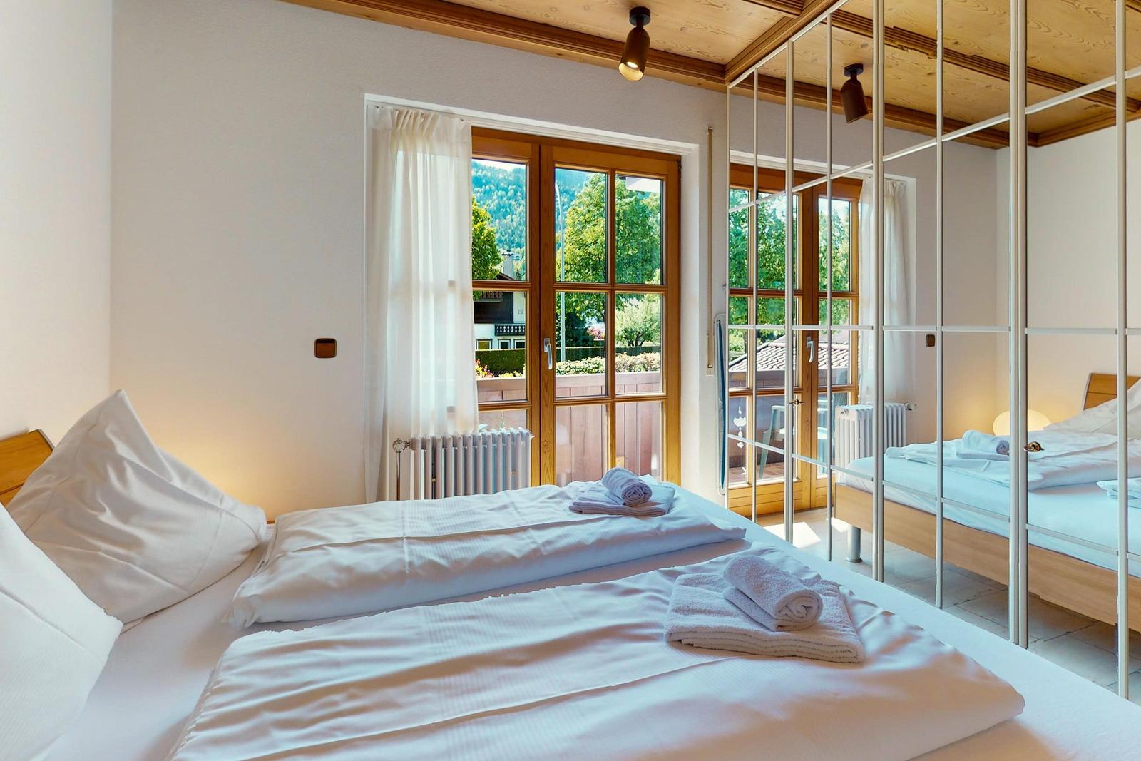Schlafzimmer mit Bett, Spiegelschrank und Fenster zum Garten.