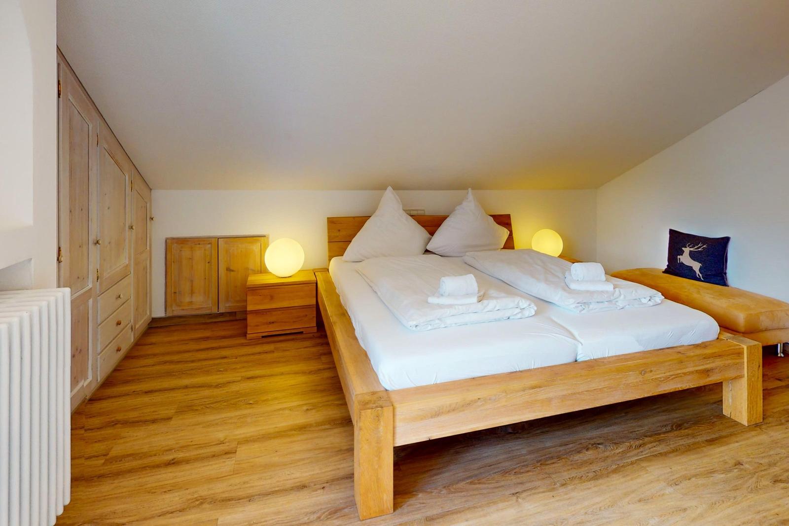 Schlafzimmer mit Holzbett, Nachttisch und Kleiderschrank. Holzfußboden und Dachschrägen.