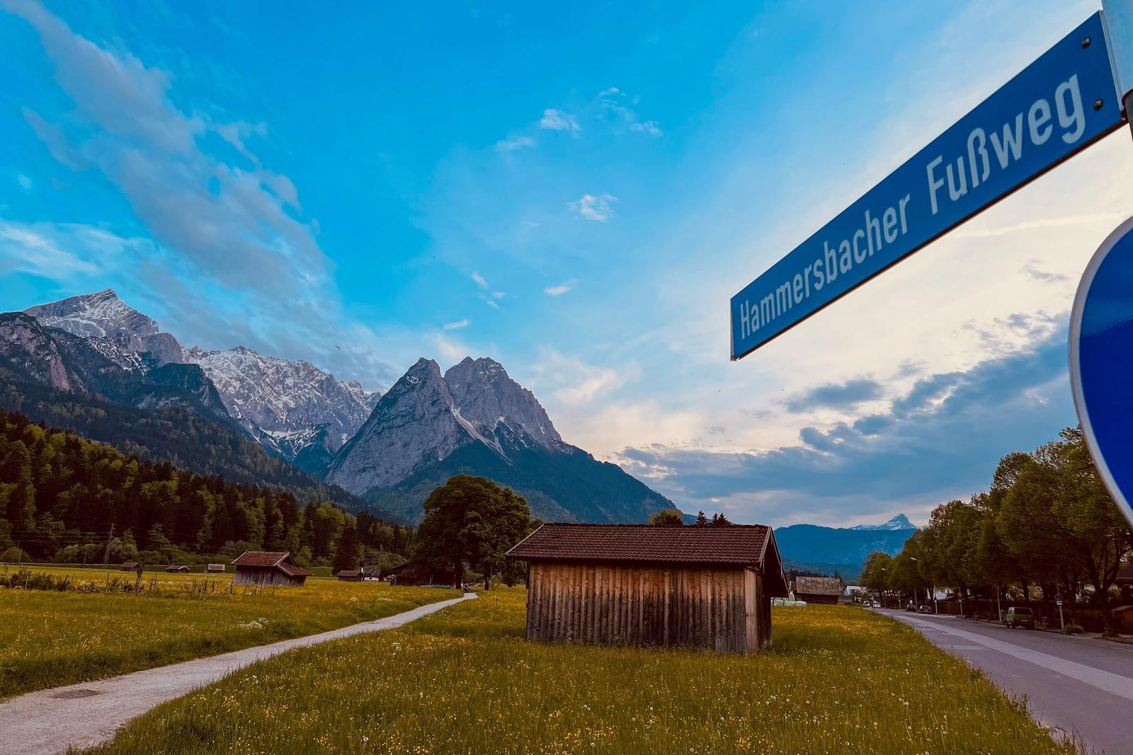Hammersbacher Fußweg führt durch grüne Wiesen mit Blick auf schneebedeckte Berge.