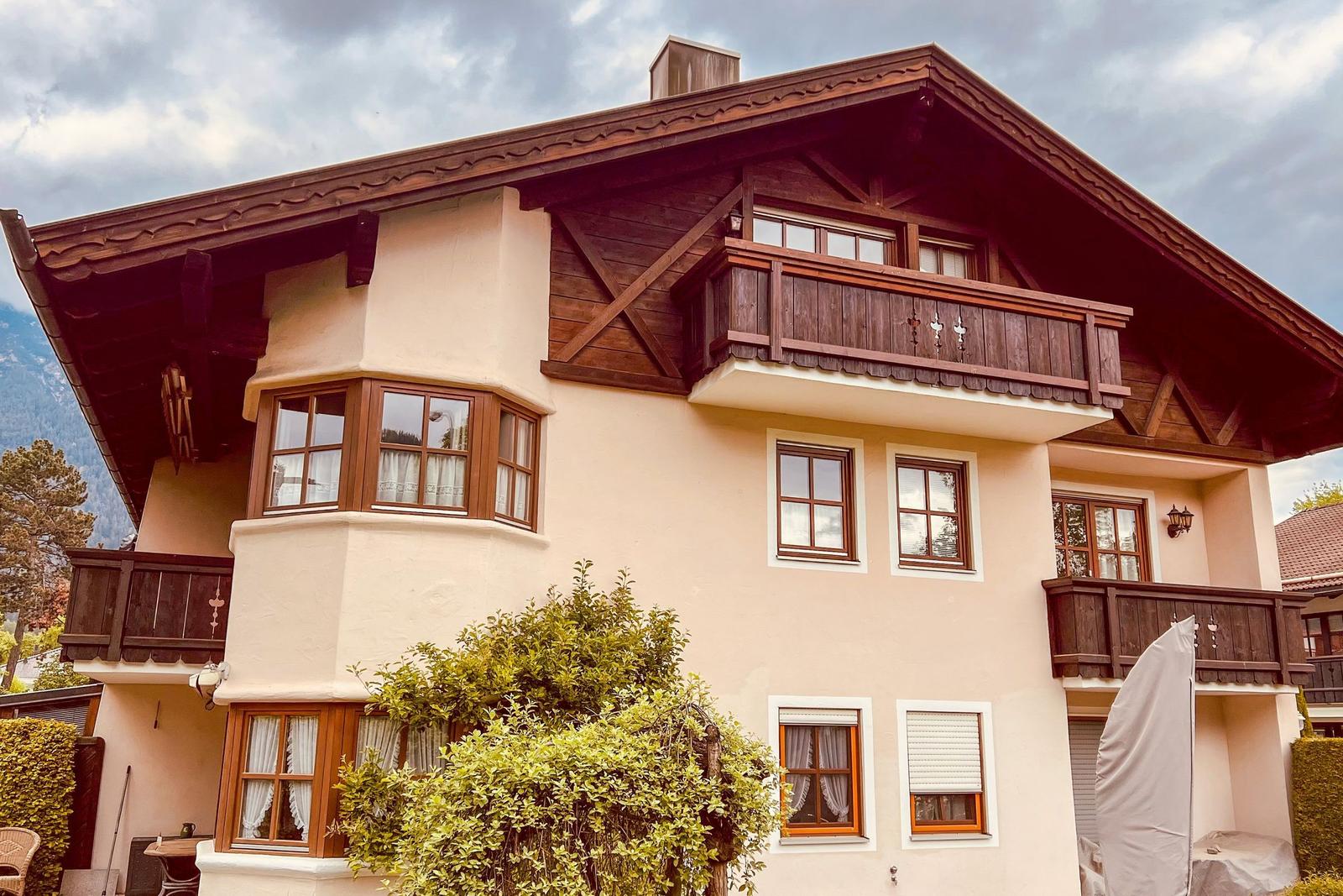 Ein zweistöckiges Haus mit Balkonen und Fenstern. Im Hintergrund sind Berge zu sehen.