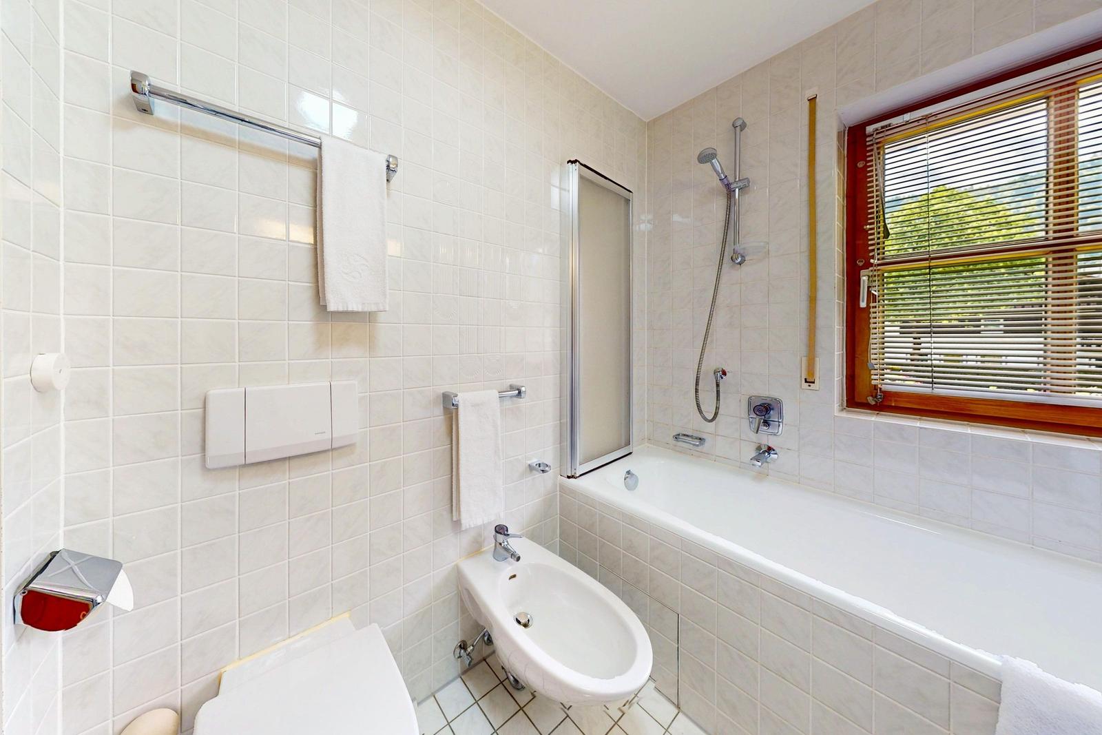 Badezimmer mit Badewanne, Dusche, Toilette und Bidet. Fenster mit Jalousie.