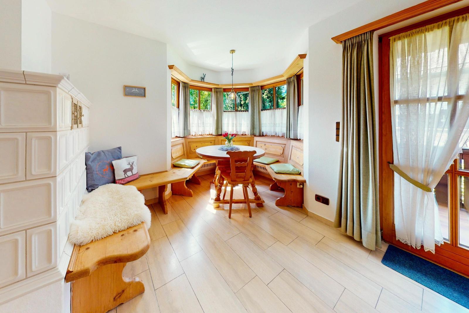 Esszimmer mit Holzbänken, runden Tisch und Fensterblick auf Grün.