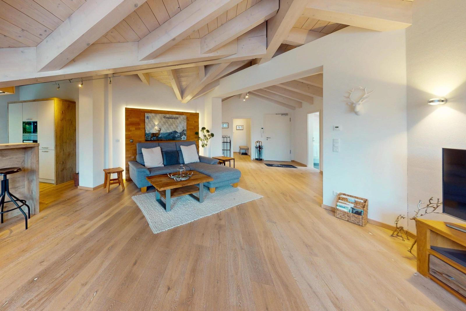 Wohn- und Küchenbereich mit Holzboden, Sofa und TV. Deckenbalken und Wanddekoration sichtbar.