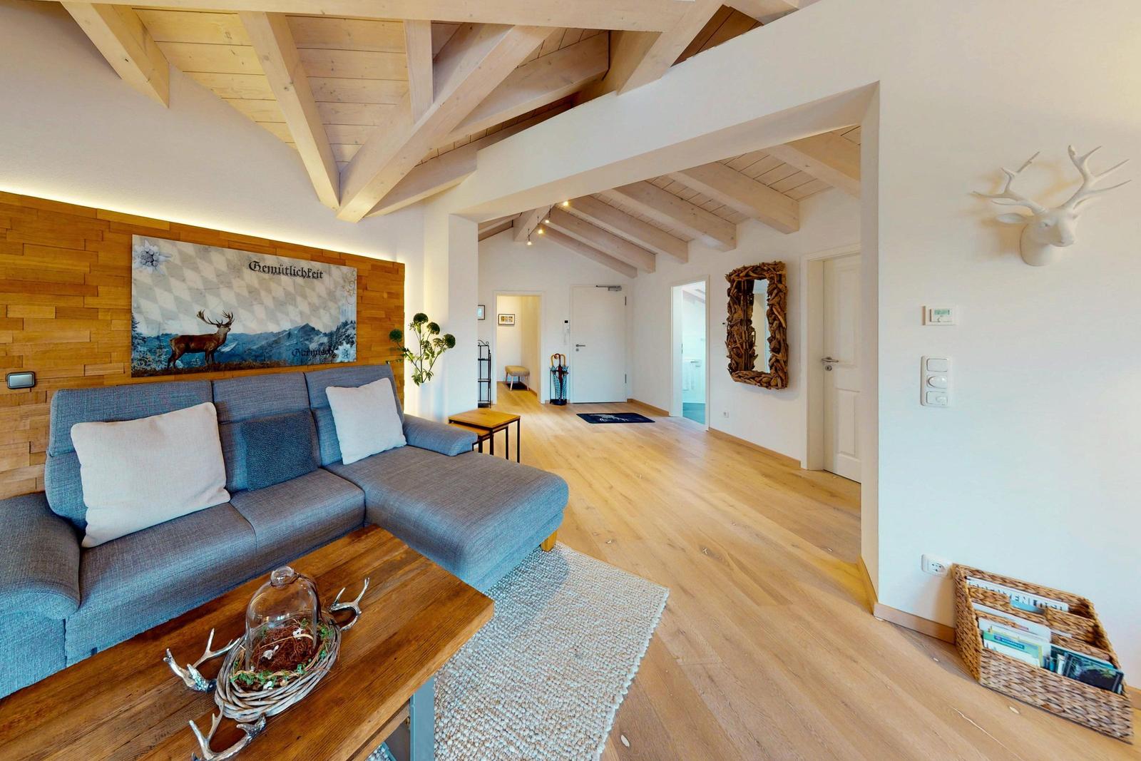 Wohnbereich mit Holzdecke, Sofa und Holzboden. Wandbild und Hirschgeweih dekorieren den Raum.