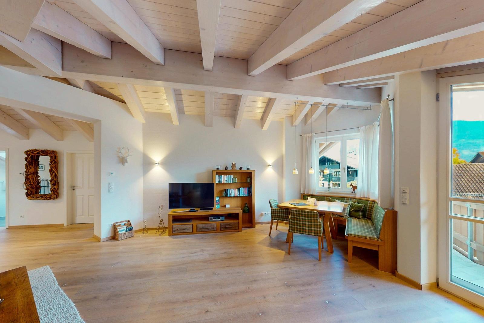 Wohn- und Essbereich mit Holzbalkendecke, TV und Tisch mit Stühlen.