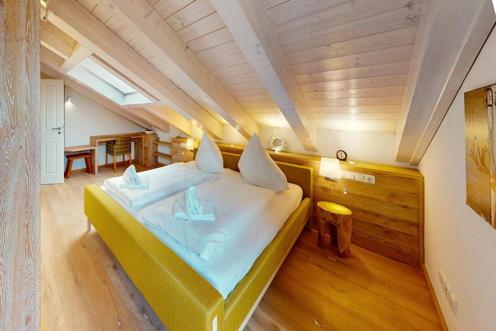 Schlafzimmer mit Dachschrägen, Bett und Schreibtisch.