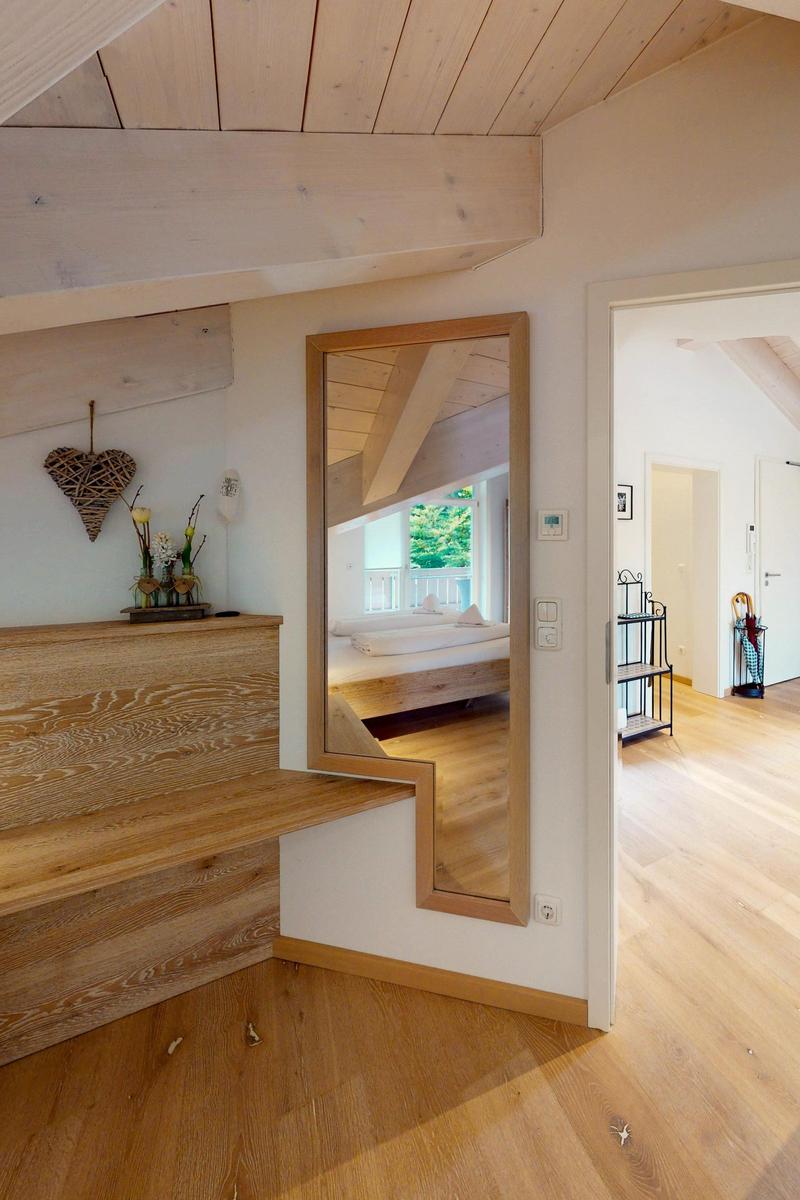 Durchgang mit Spiegel zeigt Schlafzimmer mit Bett und Balkon. Holzdecke und Boden.