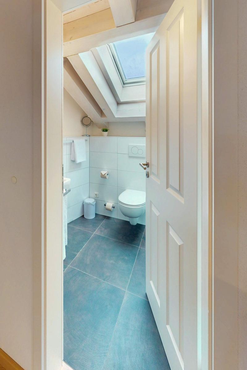 Badezimmer mit Toilette, blauen Fliesen und Dachfenster.