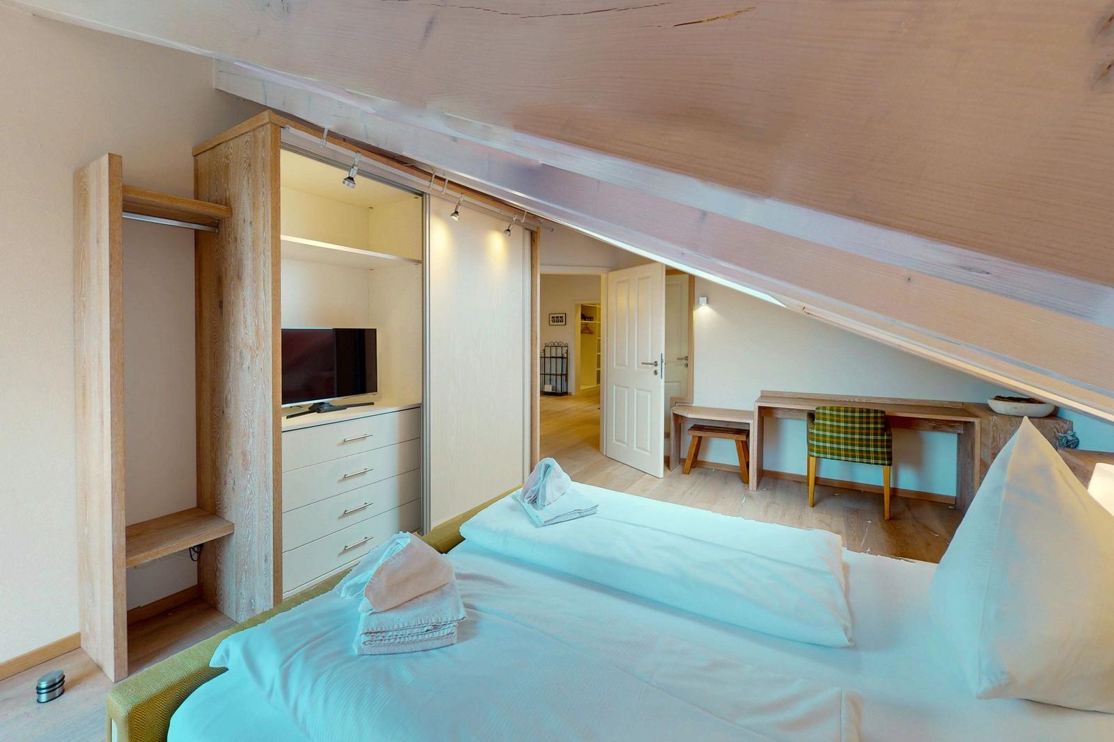 Schlafzimmer mit Bett, Kleiderschrank und Schreibtisch unter Dachschrägen.