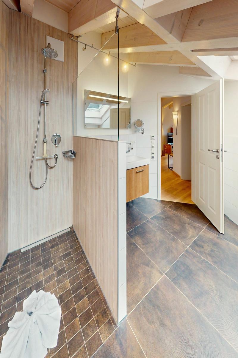 Dusche mit Glaswand, Waschbecken und Blick in das Zimmer.