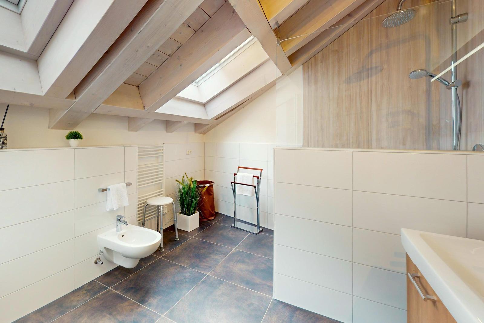 Badezimmer mit Dusche, Toilette und Waschbecken unter Holzdecke mit Dachfenster.