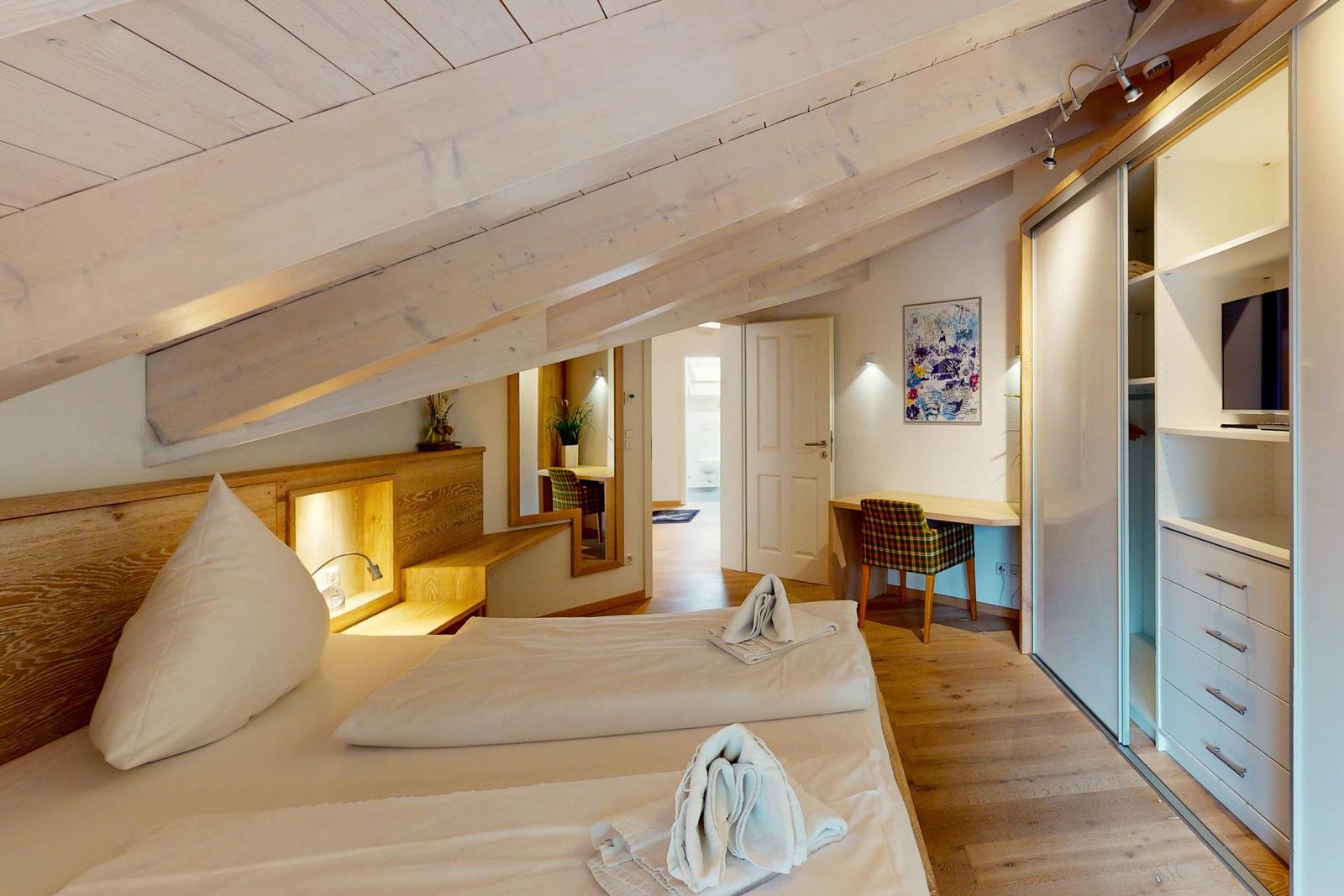 Schlafzimmer mit Dachschrägen, Bett, Schrank und Schreibtisch.