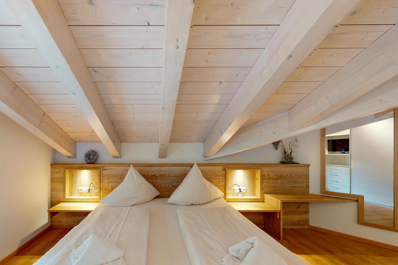 Schlafzimmer mit Holzboden, Bett und eingebauten Nachttischen mit Beleuchtung.