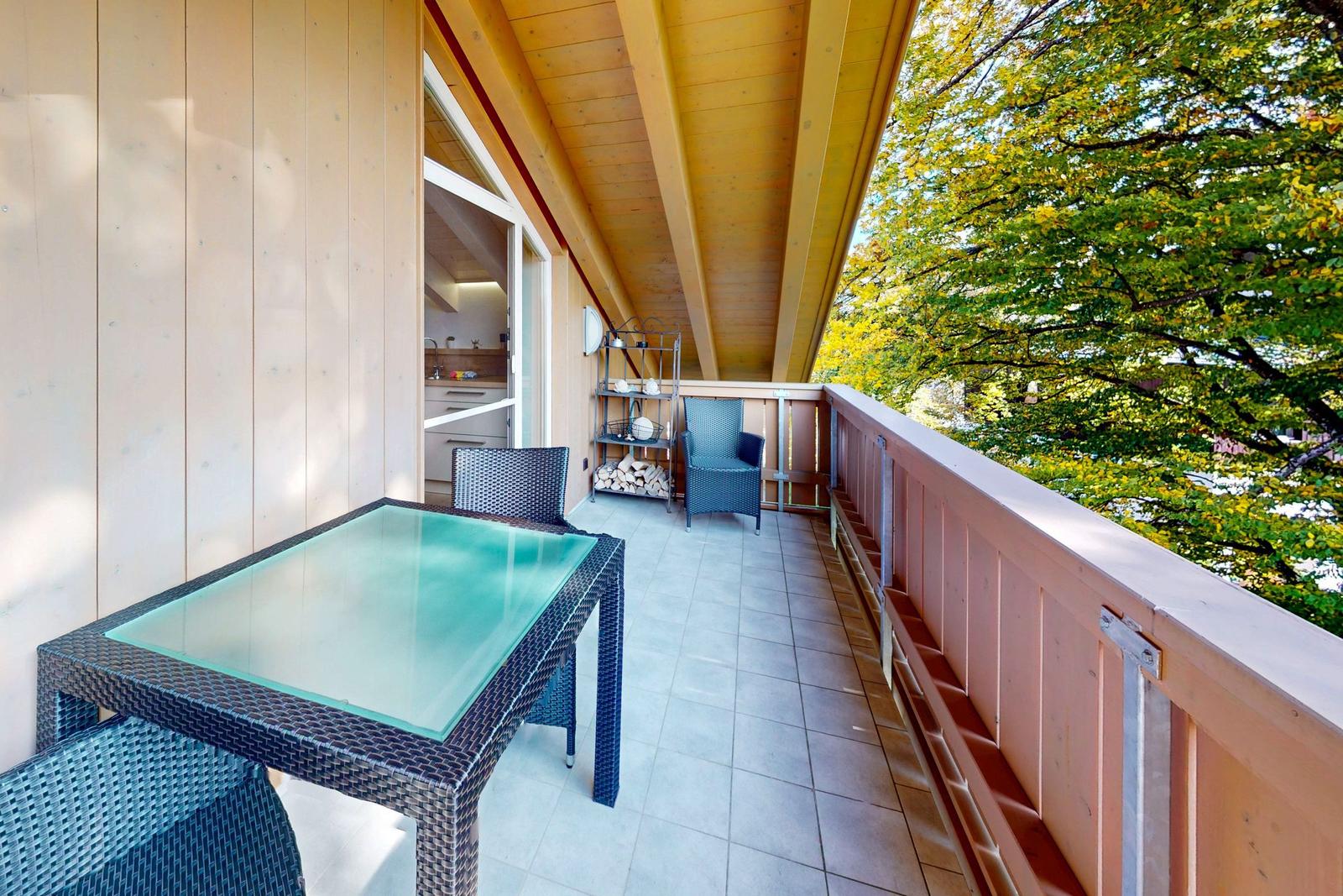 Terrasse mit Tisch, Stühlen und Blick auf Bäume. Holzverkleidung und Grillplatz.