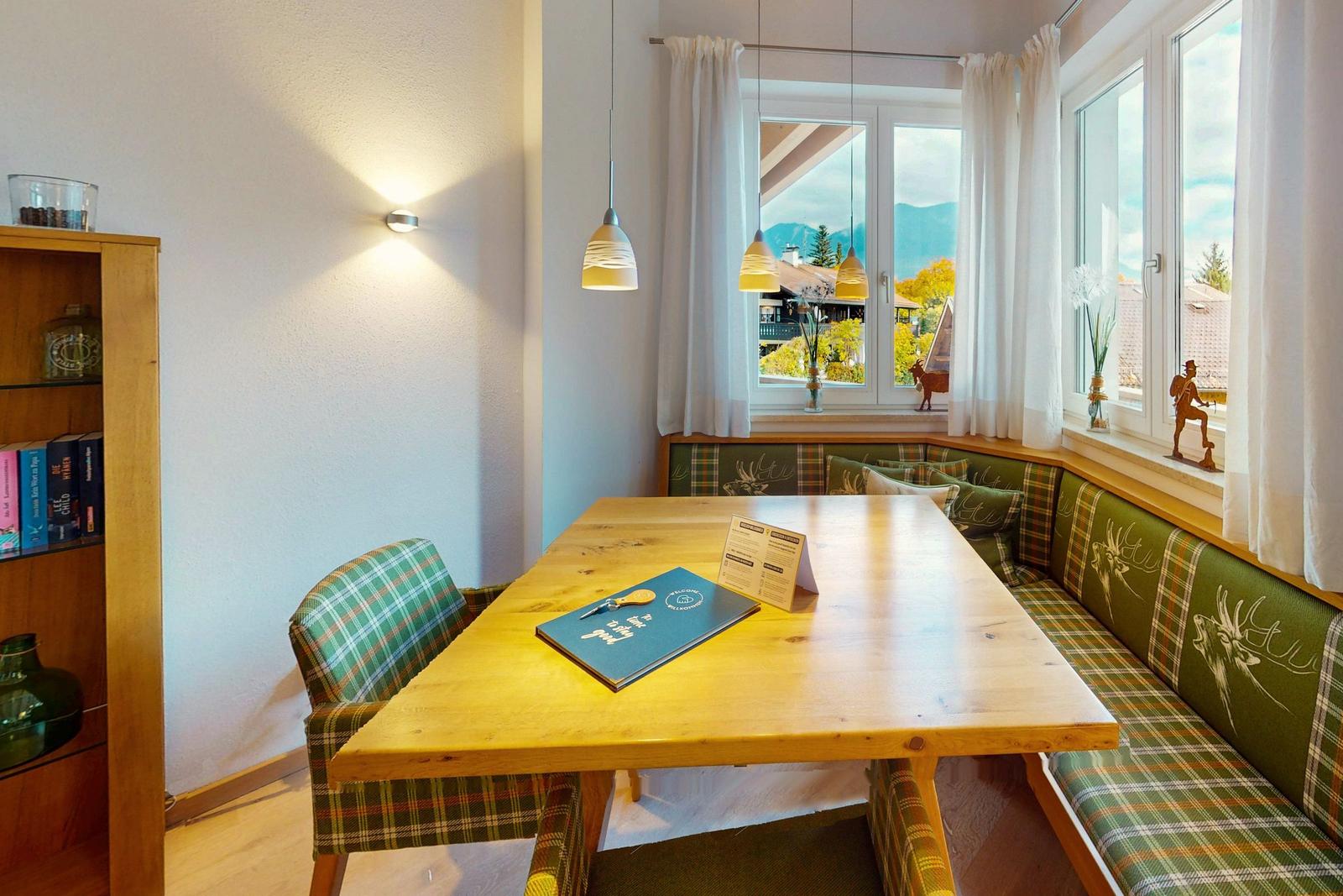 Essbereich mit Holztisch, Plaid-Sofa und Blick auf Berge.