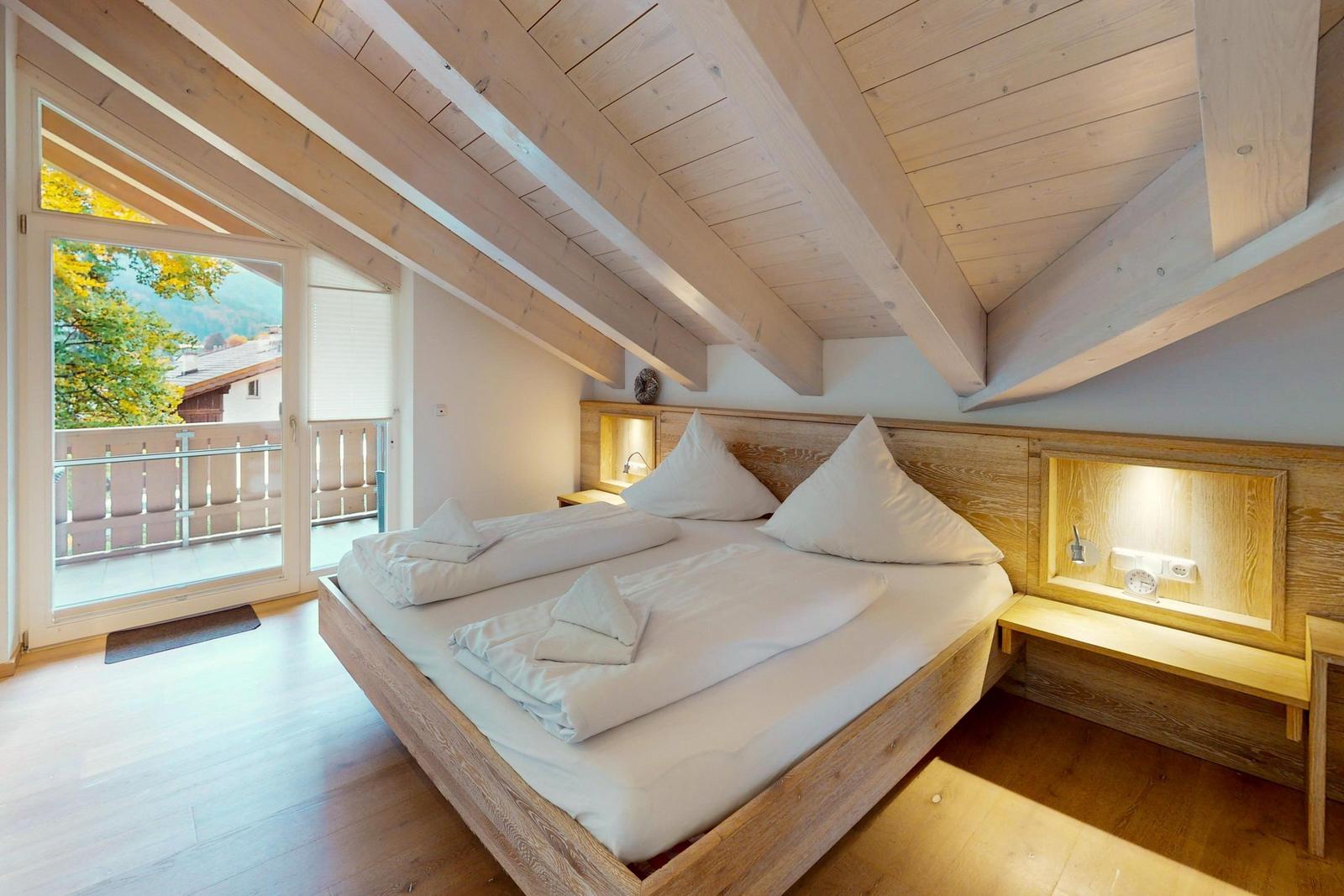 Doppelbett mit Blick auf Balkon und Wald. Holzdecke und Boden.
