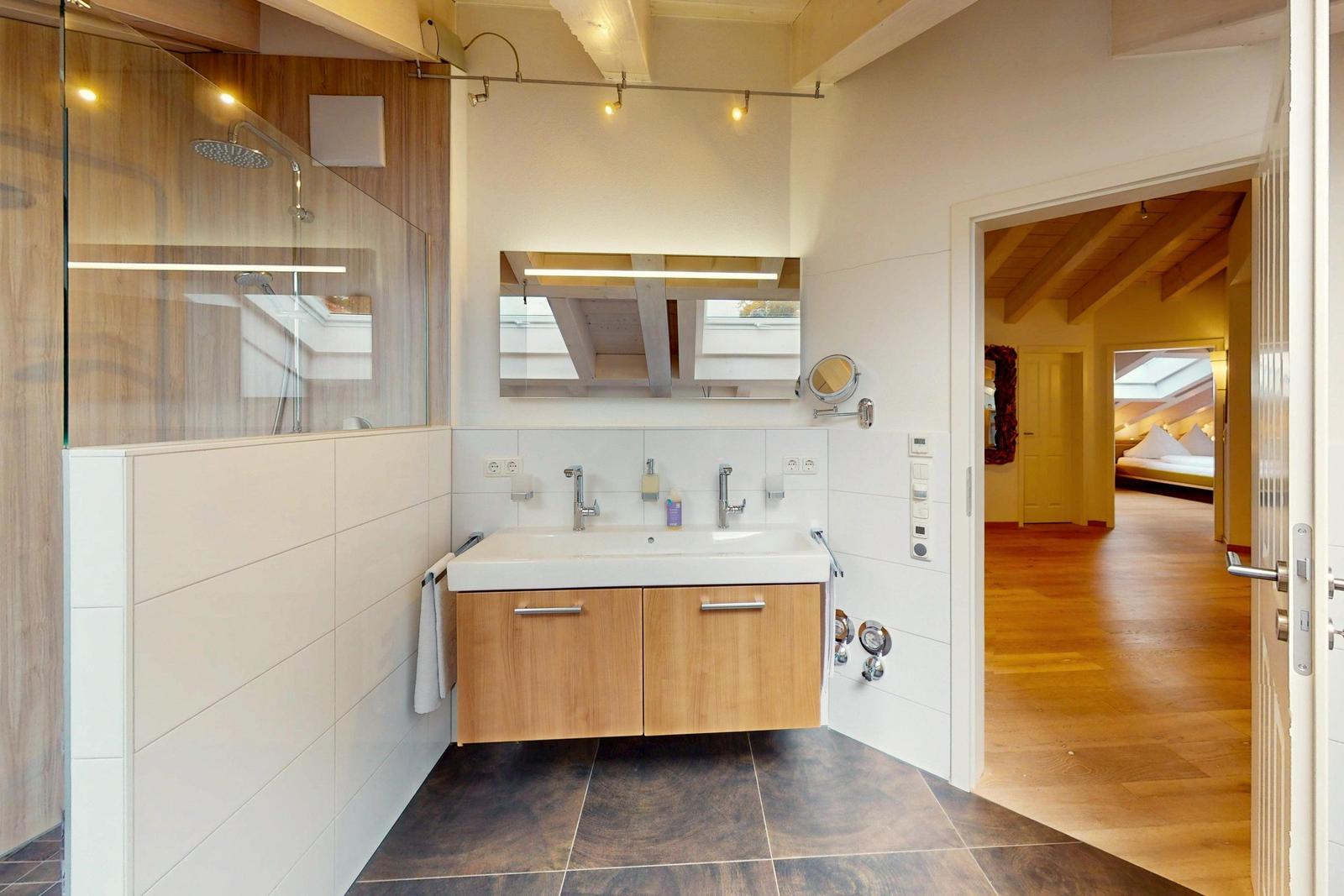 Badezimmer mit Dusche, Waschbecken und Blick in Schlafzimmer