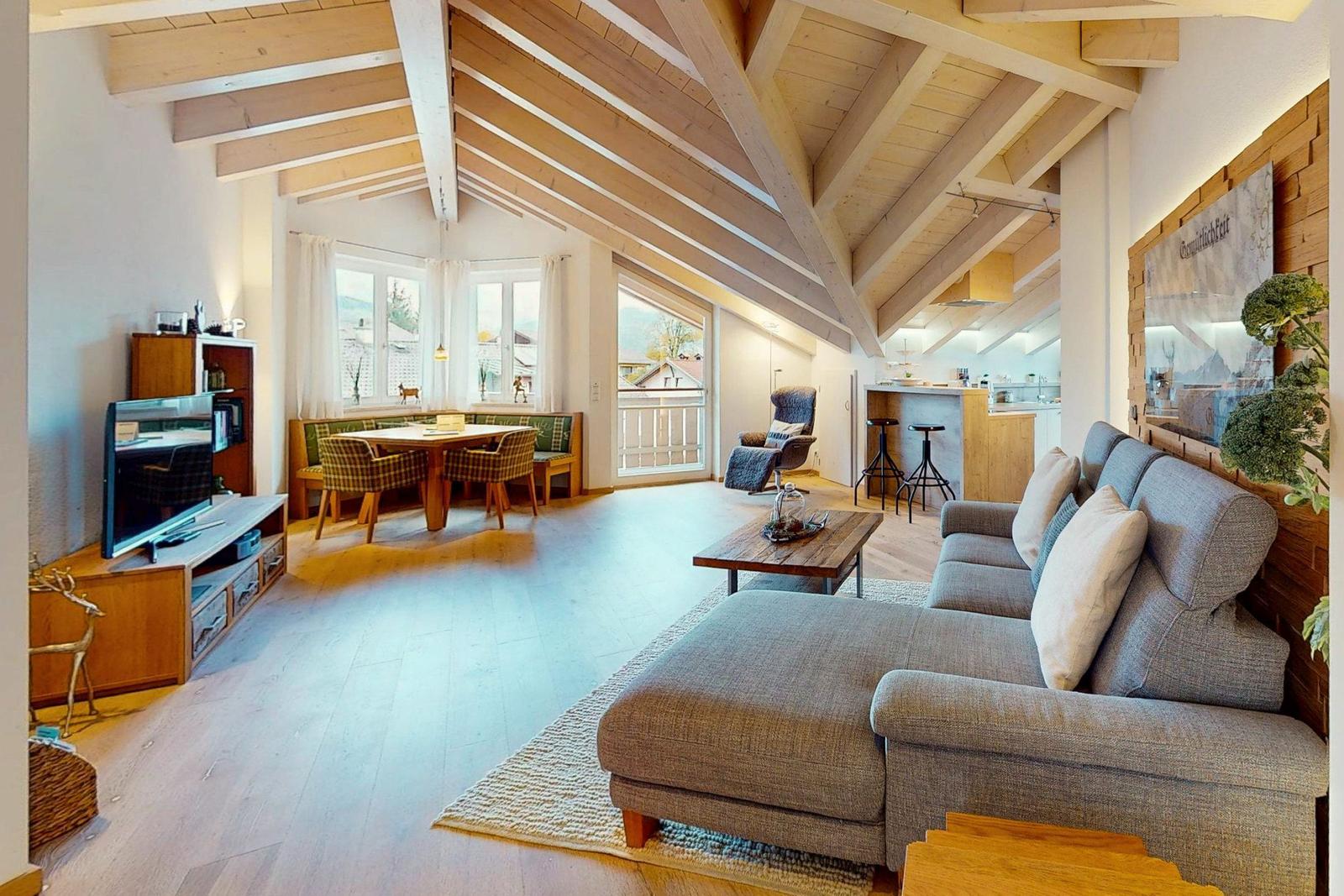 Wohn- und Essbereich mit Holzbalkendecke, Sofa, Esstisch und Küche im Hintergrund.