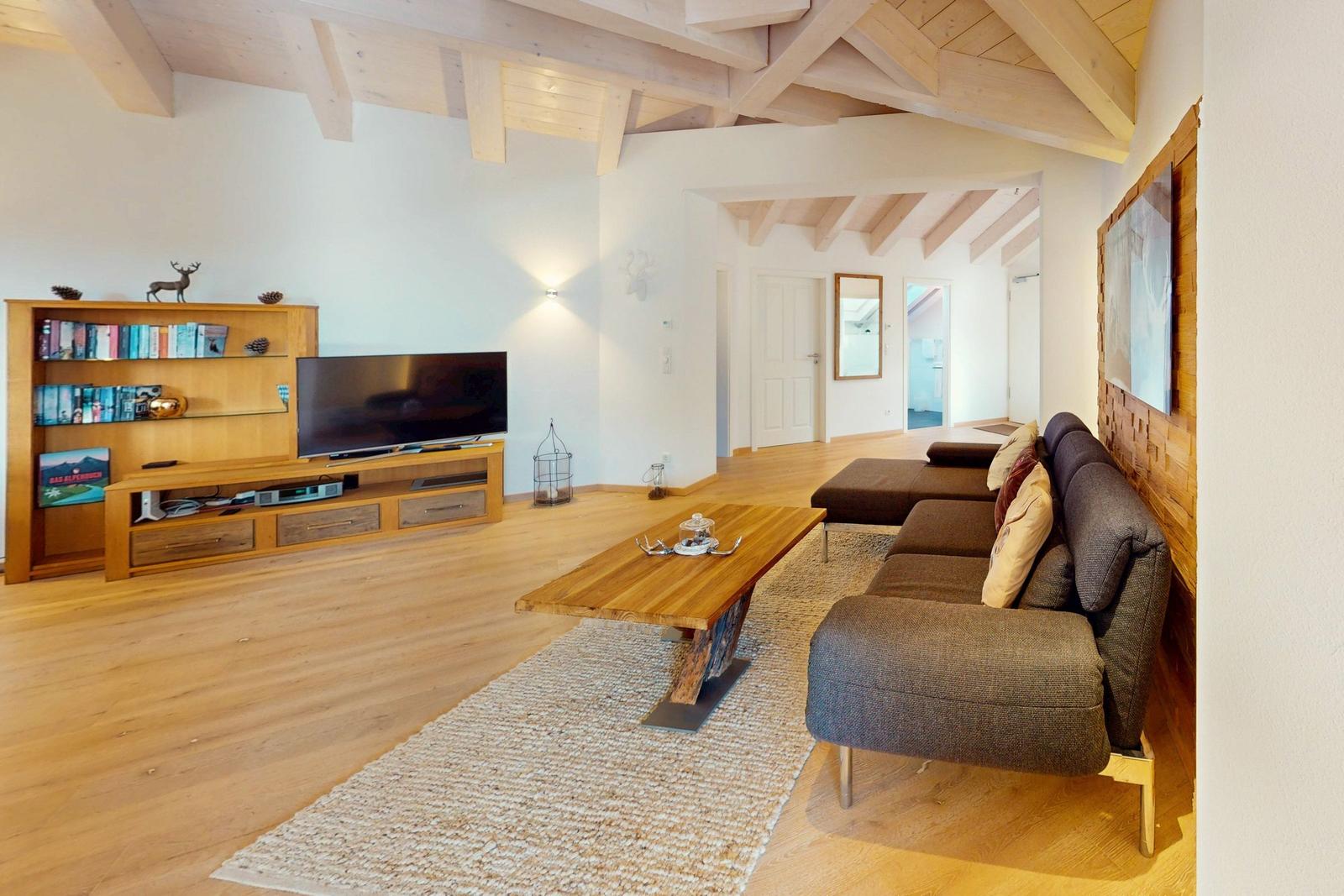 Wohnzimmer mit Holzboden, Sofa, Couchtisch und Fernseher unter Holzbalkendecke.