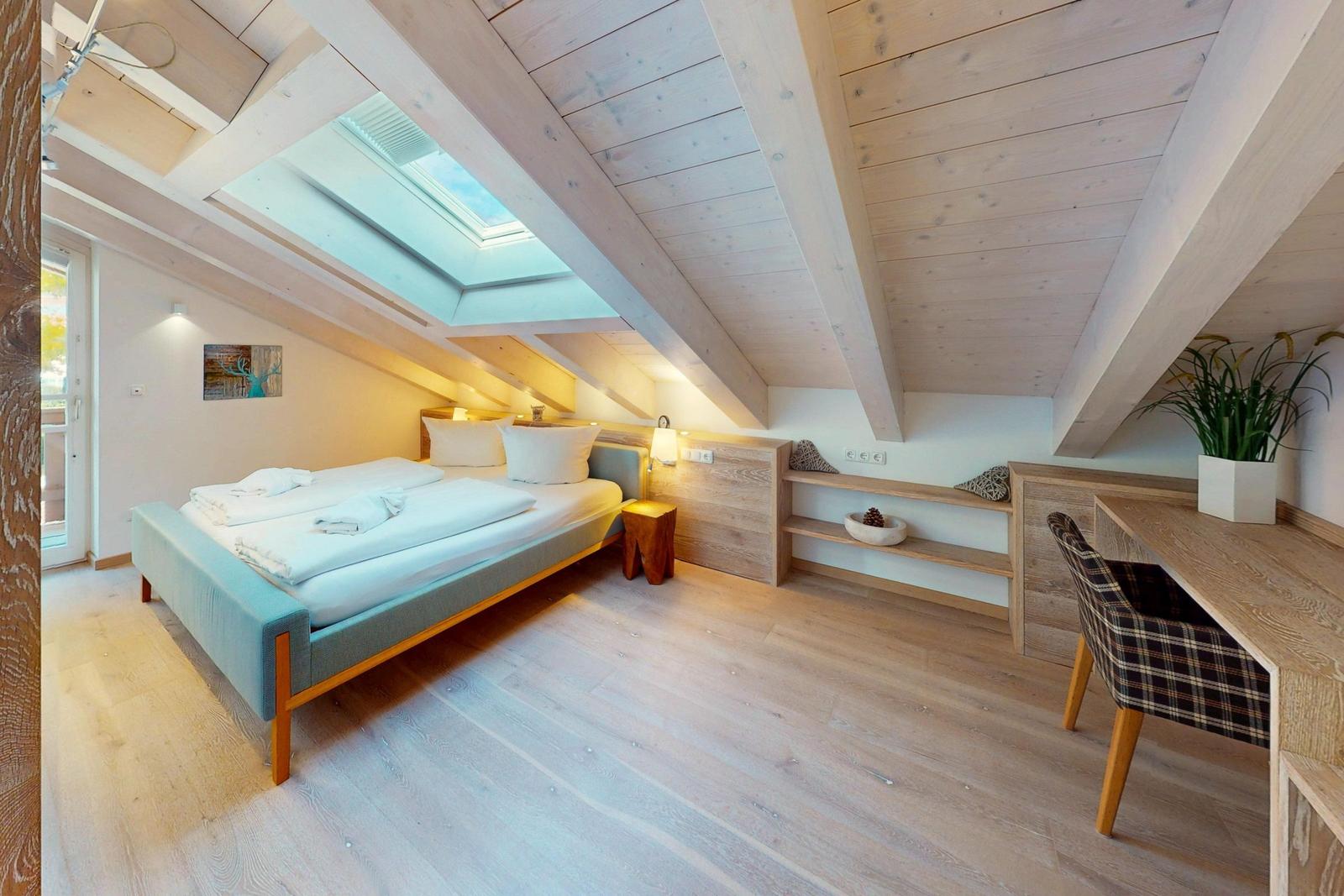 Doppelzimmer mit Dachschrägen, Bett, Schreibtisch und Dachfenster.