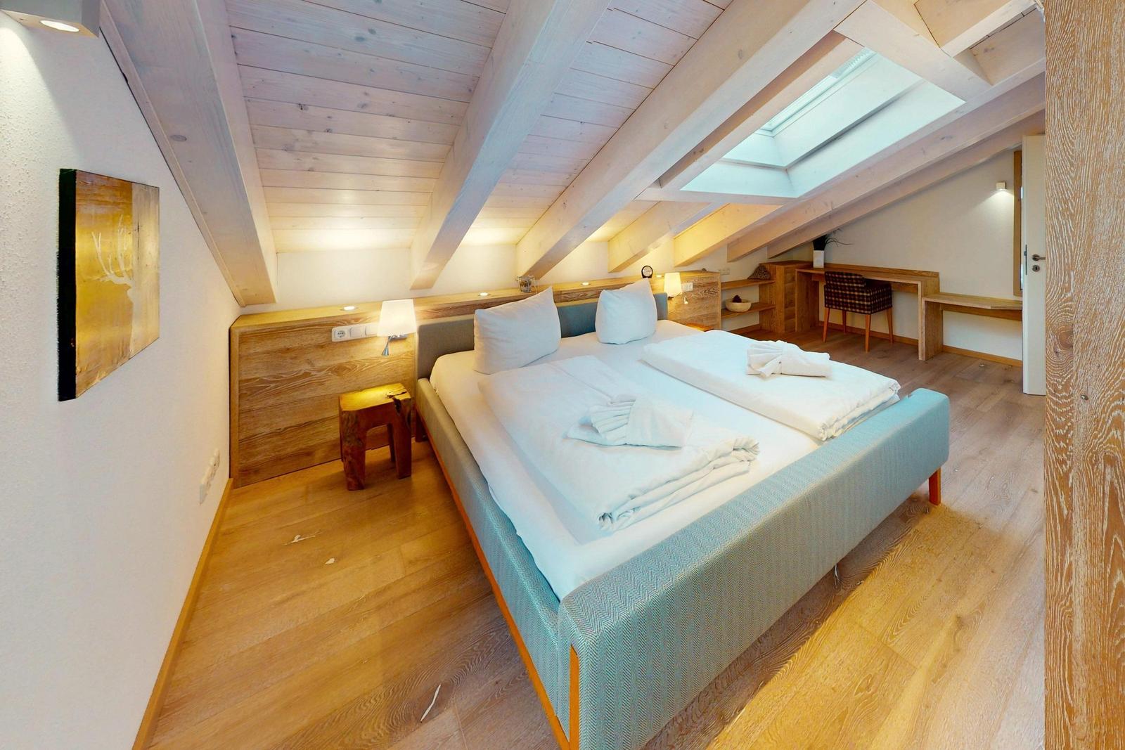 Doppelbettzimmer mit Holzdecke, Dachfenster und Schreibtisch.