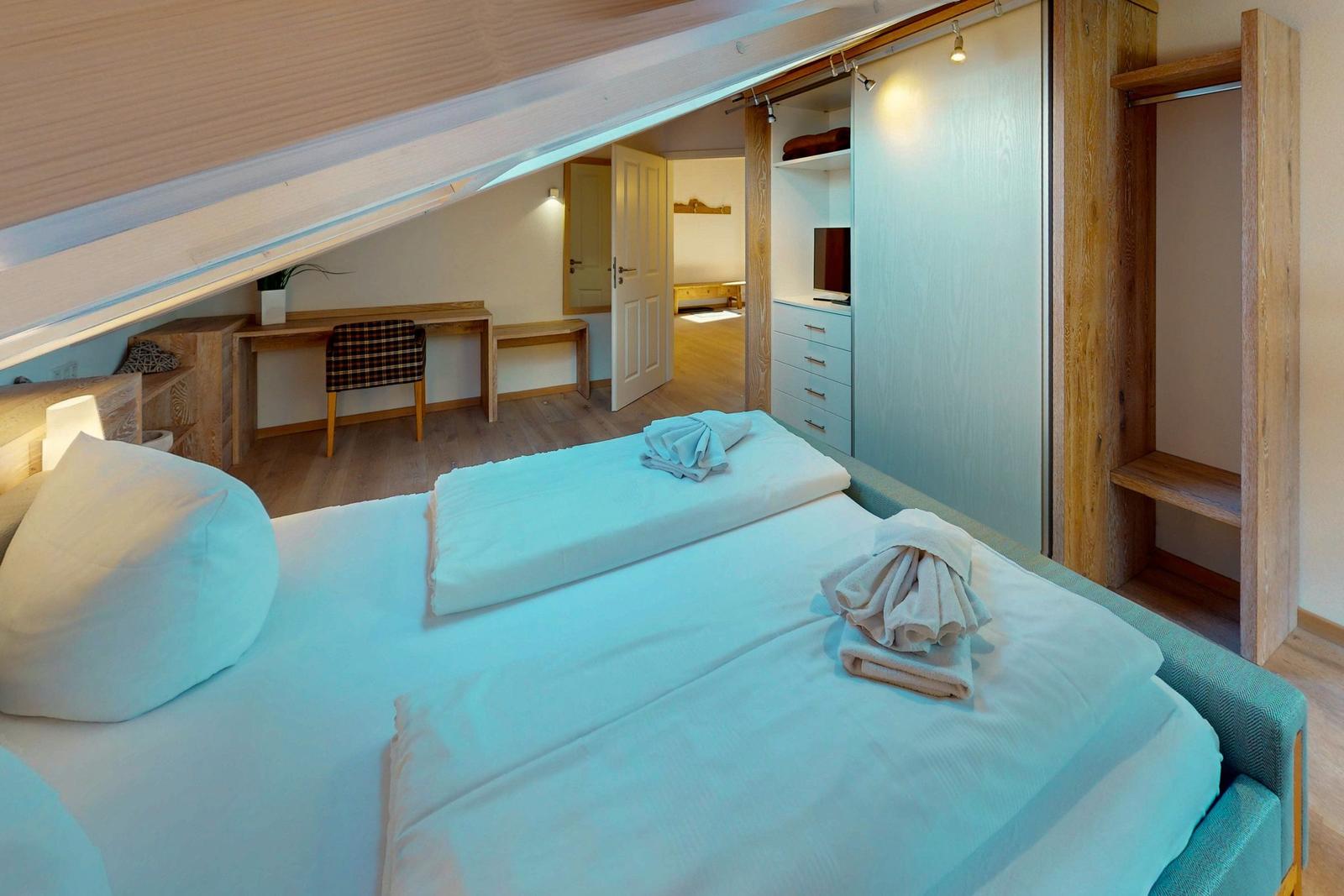 Schlafzimmer mit Doppelbett, Kleiderschrank und Schreibtisch unter Dachschrägen.