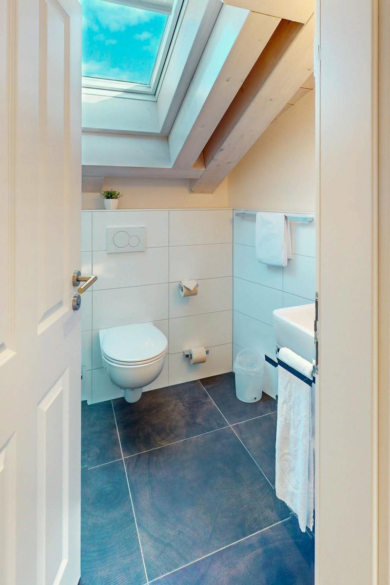 Badezimmer mit Toilette, Waschbecken und Dachfenster. Holzbalken und weiße Fliesen.