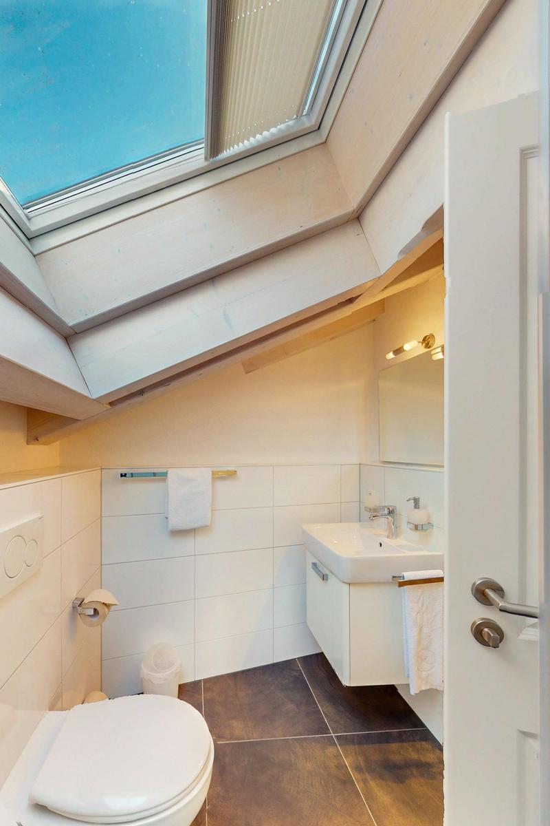 Badezimmer mit Dachfenster, Waschbecken und Toilette. Holzdecke und Fliesenboden.