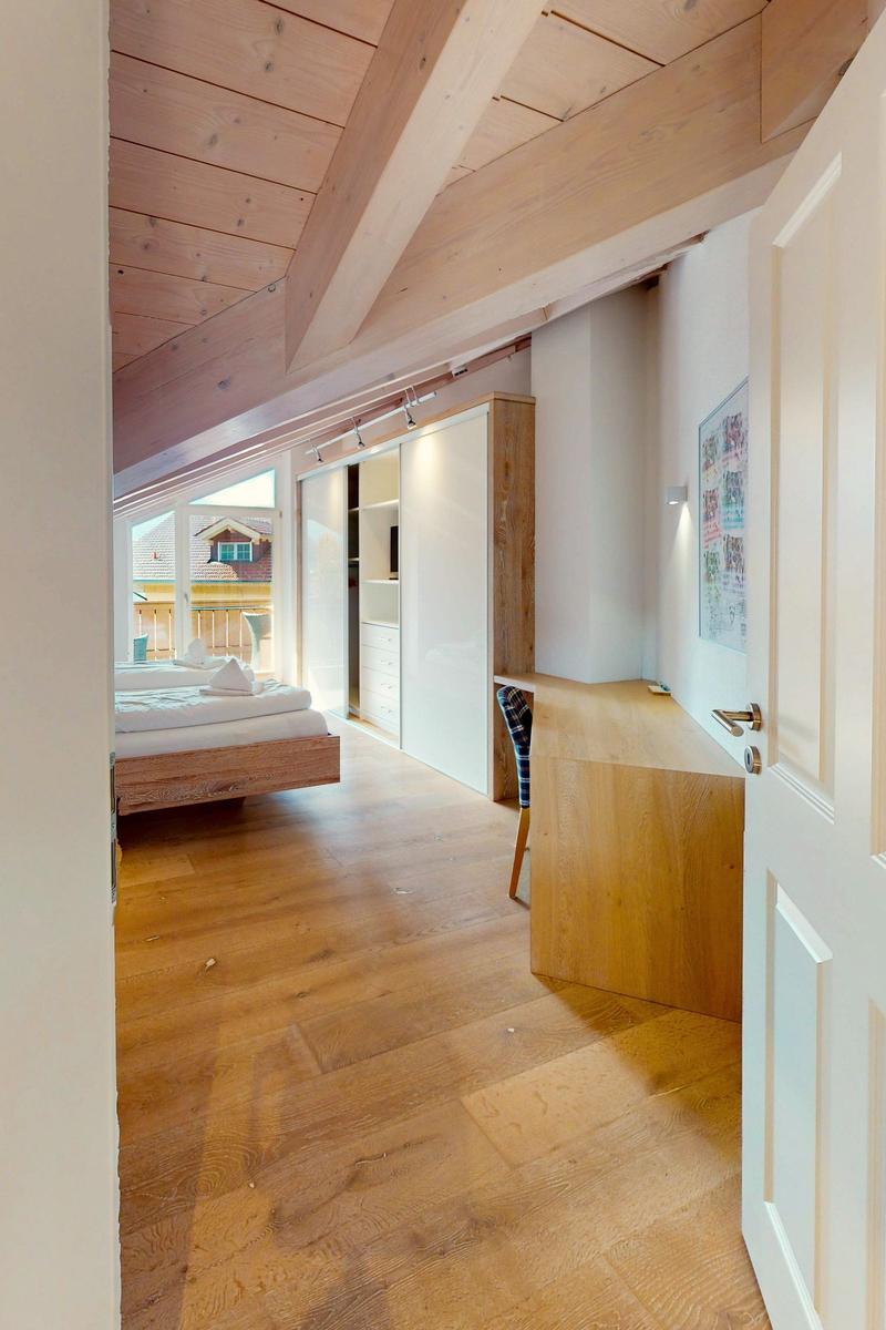 Schlafzimmer mit Holzboden, Bett, Schrank und Schreibtisch. Dachboden mit Holzdecke und Fenster.