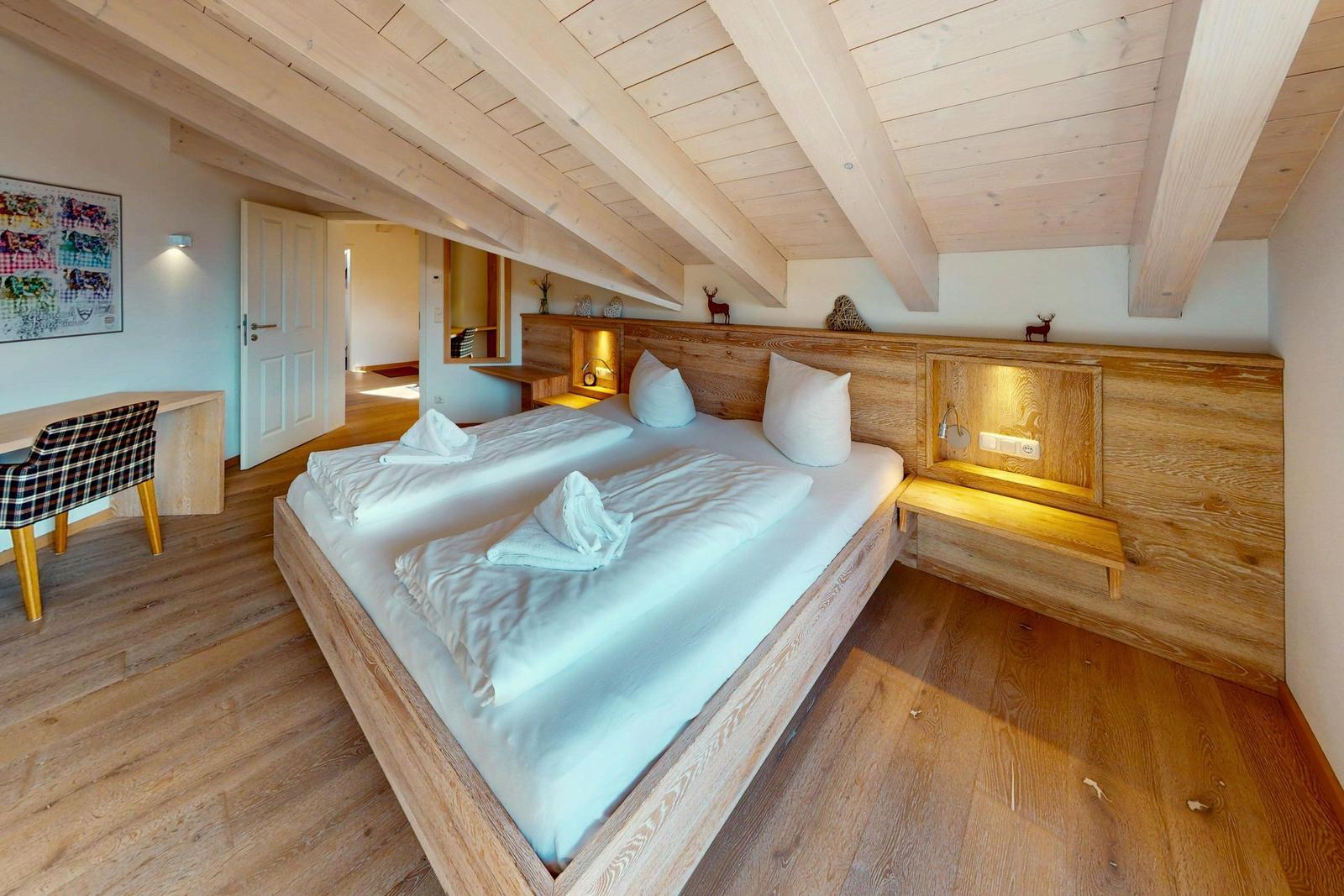 Schlafzimmer mit Holzbett, Deckenbalken und Schreibtisch mit Stuhl.