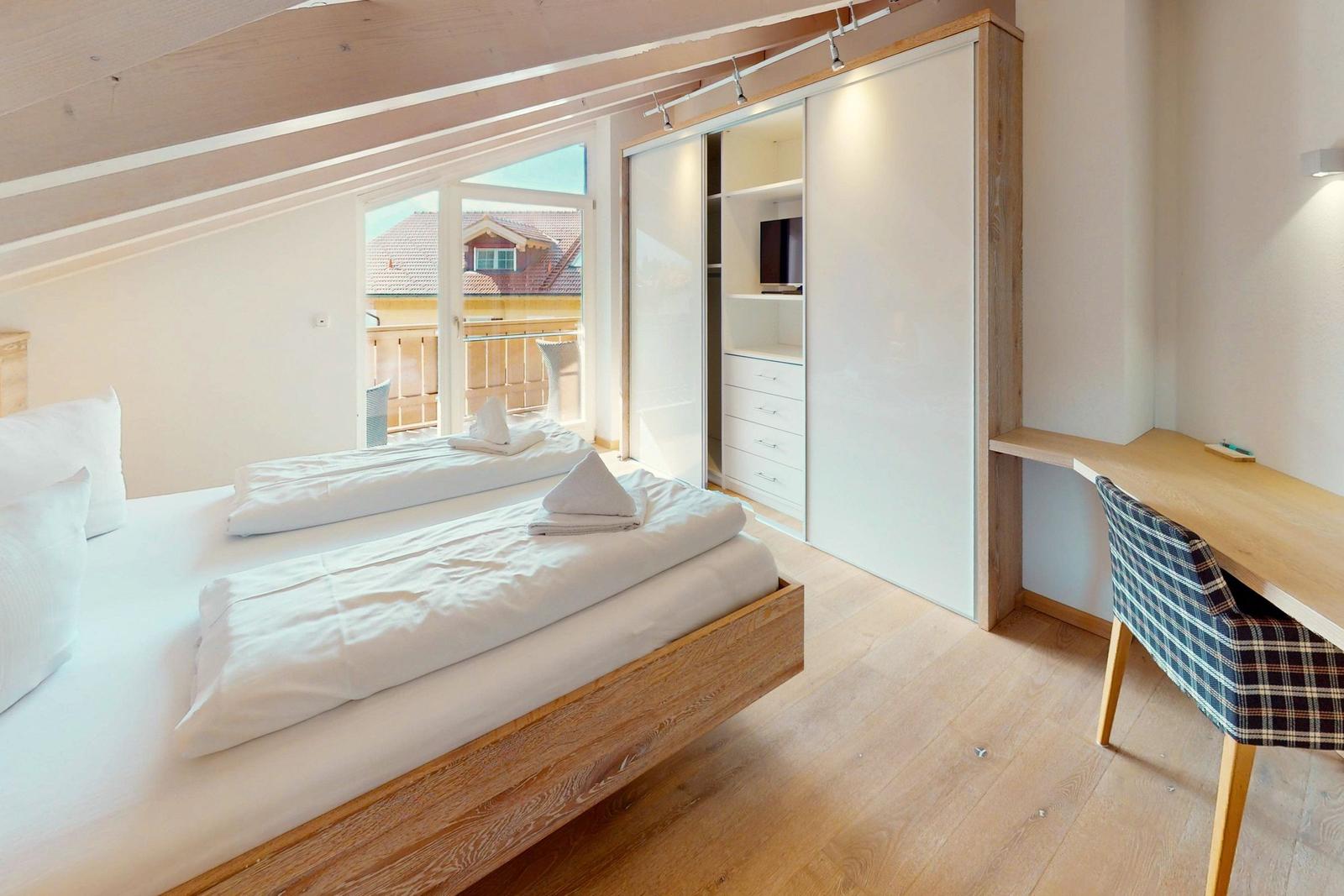 Schlafzimmer mit Doppelbett, Schwebetüren-Schrank und Schreibtisch mit Stuhl.