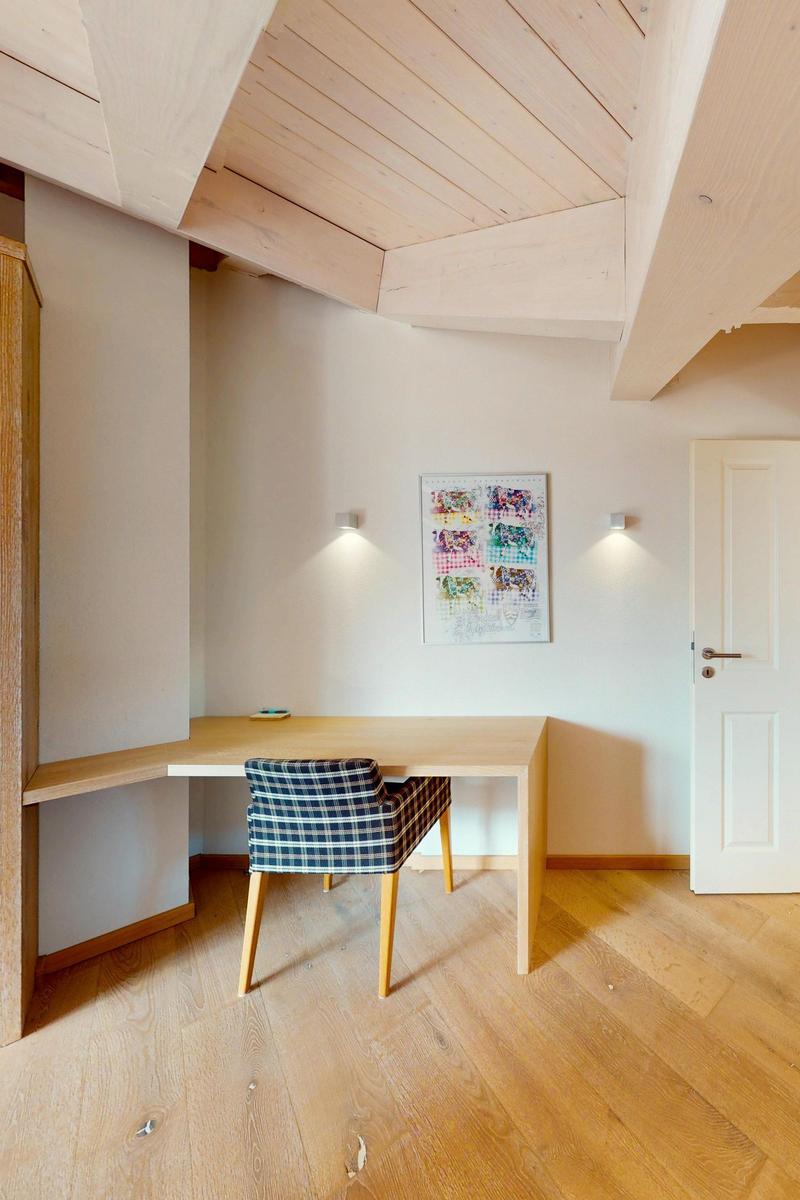 Ein Schreibtisch mit Stuhl unter Holzdecke und Wandbild.